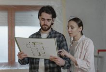 Duas pessoas analisam uma planta de reforma residencial em um ambiente interno.
