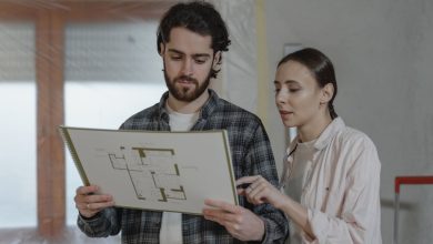 Duas pessoas analisam uma planta de reforma residencial em um ambiente interno.