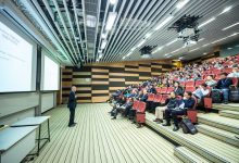 Palestrante apresenta conteúdo em um auditório moderno diante de uma plateia atenta.