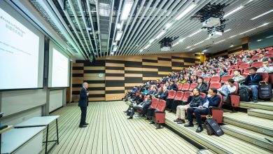 Palestrante apresenta conteúdo em um auditório moderno diante de uma plateia atenta.