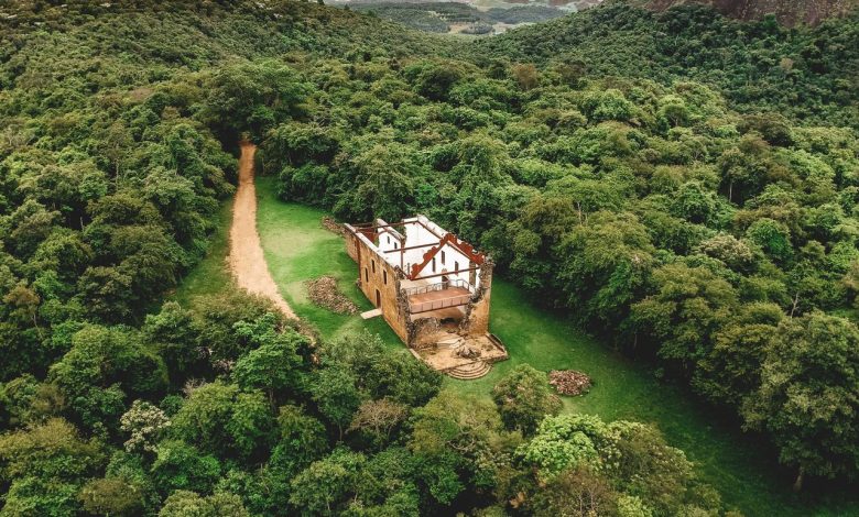 Vista aérea de um templo histórico em restauração, cercado por árvores e montanhas, com um caminho atravessando o gramado.
